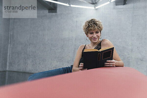 Lächelnde Frau liest ein Buch auf dem Sofa