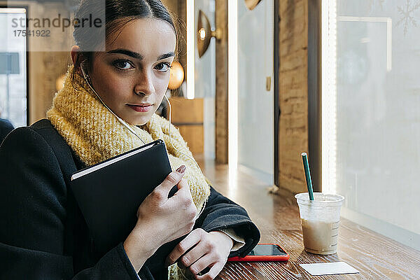 Confident teenage girl with diary in cafe