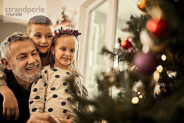 Grandchildren with grandfather looking at decorated christmas tree at home
