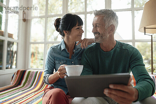 Smiling man with tablet PC by woman holding coffee cup on sofa