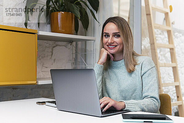 Schöne Geschäftsfrau mit der Hand am Kinn sitzt mit Laptop im Studio