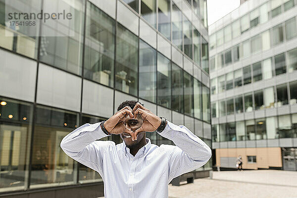 Young man making heart shape in front of building