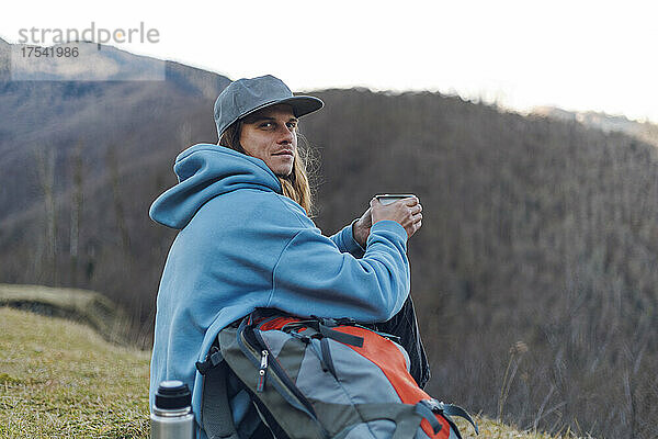 Wanderer mit Rucksack und Kaffeetasse am Berg