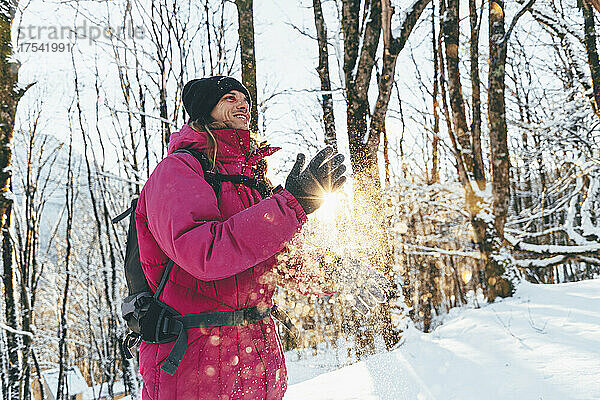 Lächelnder Tourist  der im Wald Schnee von den Händen wischt