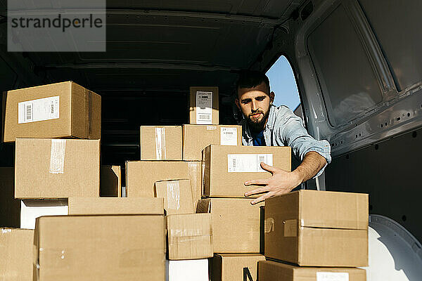 Man arranging brown boxes in van on sunny day