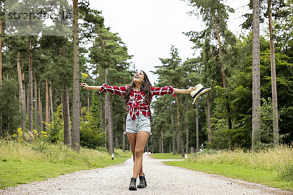Cheerful woman with arms outstretched standing on road amidst trees at Cannock Chase