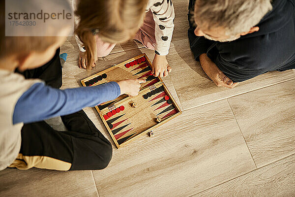 Children playing backgammon with grandfather at home
