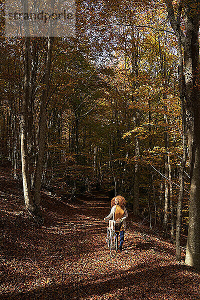 Junge Frau mit Fahrrad auf Fußweg im Herbstwald