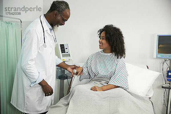 Lächelnder Patient mit Oximeter blickt Arzt im Krankenhaus an