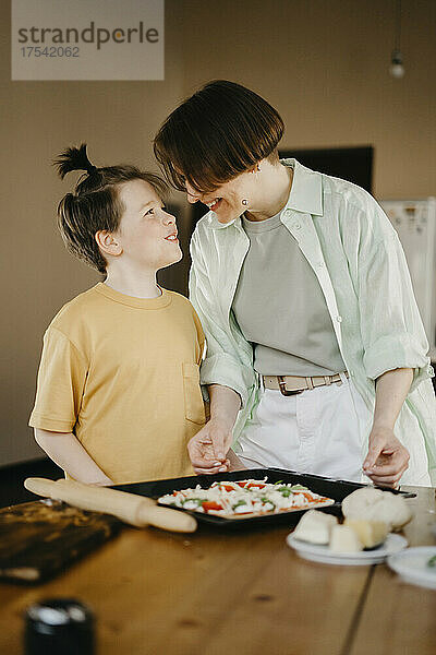Smiling son looking at mother preparing pizza on table