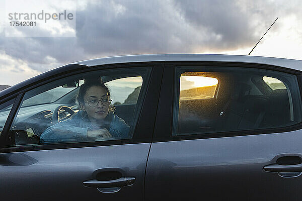 Junge Frau blickt bei Sonnenuntergang durch das Autofenster