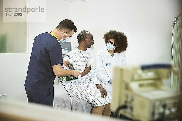 Krankenschwester mit Sauerstoffgerät durch Patient im Gespräch mit Arzt im Krankenzimmer