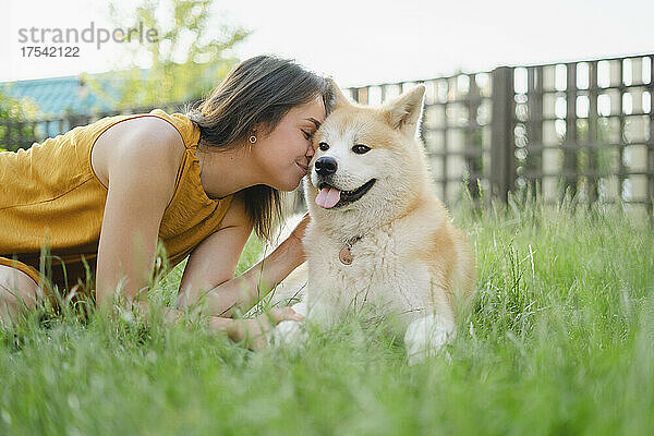 Woman kissing her Akita dog on grass
