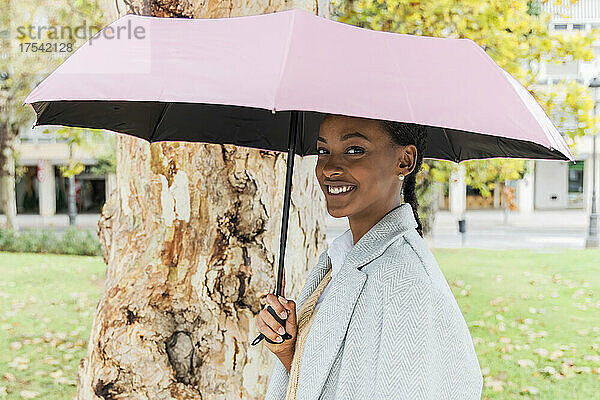 Smiling girl with umbrella by tree in park