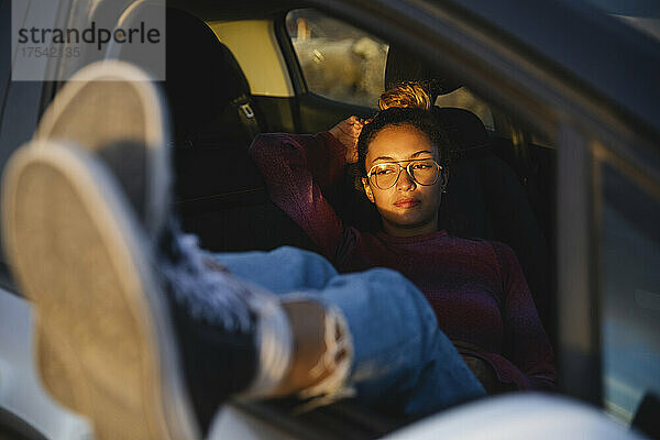 Young woman resting in car at sunset