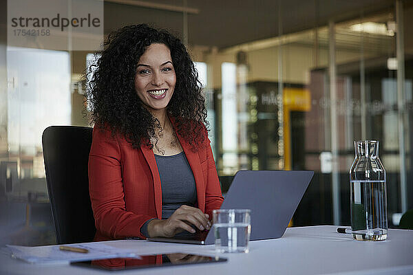 Glückliche Geschäftsfrau sitzt mit Laptop am Schreibtisch im Büro