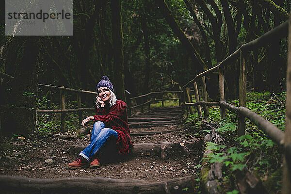 Lächelnde Frau sitzt auf Holzweg im Wald