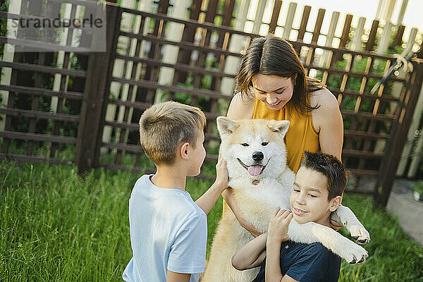 Glückliche Familie  die mit Akita-Hund auf Gras spielt