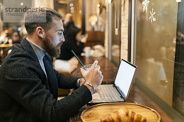 Freelancer using laptop and drinking iced coffee at restaurant