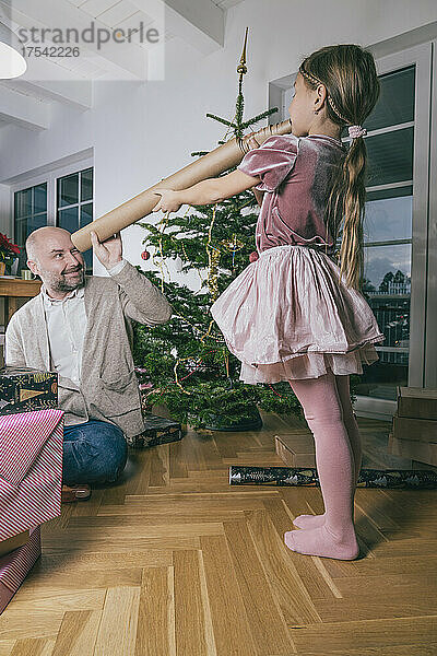 Father looking at daughter through rolled up wrapping paper at home