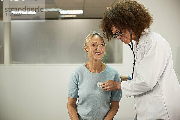 Arzt mit lockigem Haar untersucht älteren Patienten im Krankenzimmer