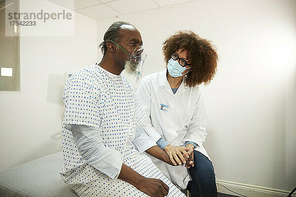 Der Arzt trägt eine schützende Gesichtsmaske und sitzt mit dem Patienten zusammen  der durch einen Vernebler inhaliert  im Krankenzimmer