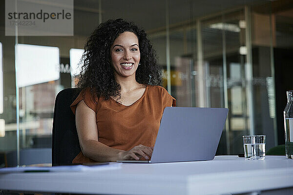 Happy businesswoman with laptop on desk at workplace