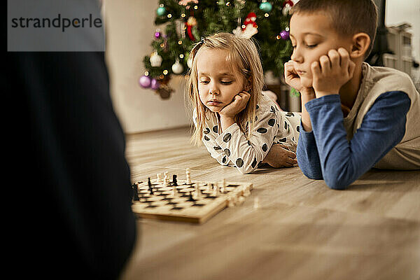 Boy and girl lying on floor looking at chess board at home