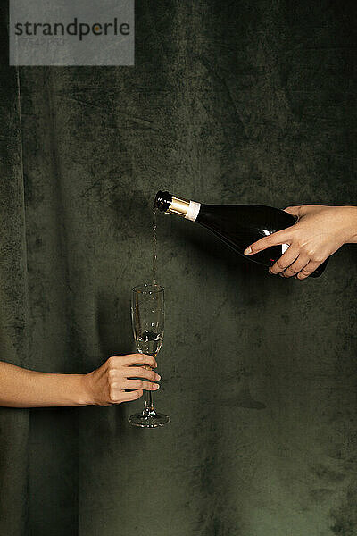 Hand pouring champagne in flute held by woman in front of black curtain