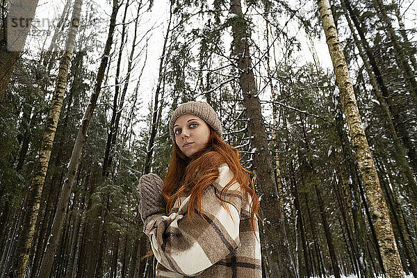 Selbstbewusste rothaarige Frau vor Bäumen im Wald