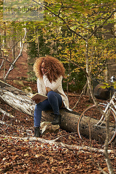 Woman reading book sitting on log in autumn forest