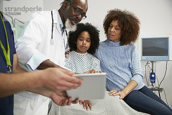 Arzt bespricht die Behandlung am Tablet-PC mit Patientin und Mutter im Krankenhaus