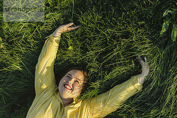 Happy woman with arms raised lying on grass