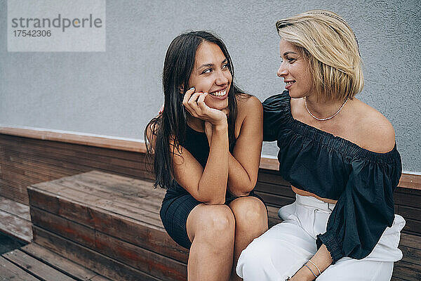 Woman with arm around friend sitting on bench in front of wall