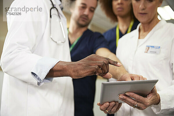 Arzt gestikuliert in der Nähe von Kollegen mit Tablet-PC bei Besprechung im Krankenhaus