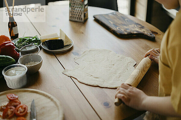 Boy preparing pizza dough with rolling pin on table