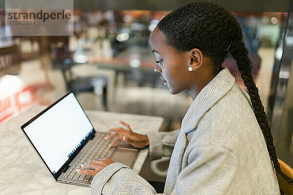 Teenage girl using laptop at table in cafe