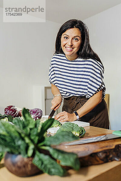 Smiling woman cutting broccoli on cutting board at home