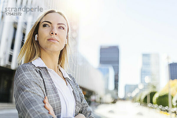 Confident businesswoman wearing wireless in-ear headphones