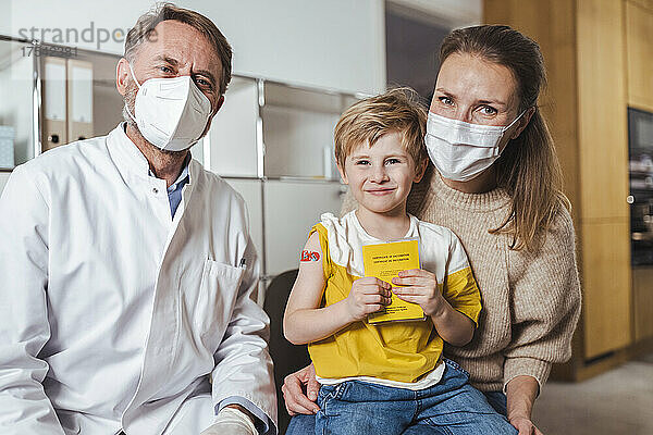 Lächelnder Junge mit Impfpass  Arzt und Mutter in der Mitte