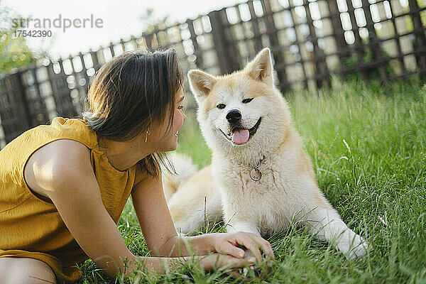 Verspielte Frau blickt auf Akita-Hund  der auf Gras sitzt