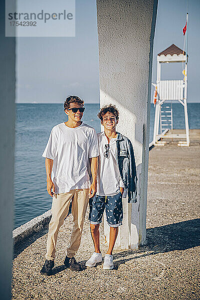 Smiling brothers standing on pier in front of sea