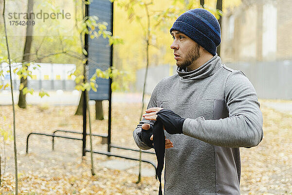 Young man with knit hat wrapping bandage on hand at park