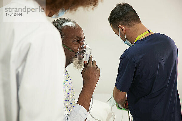 Patient trägt Sauerstoffmaske mit medizinischem Personal im Krankenzimmer