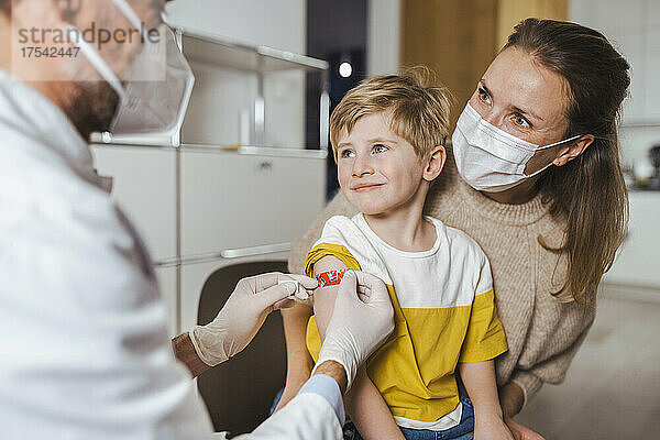 Der Arzt legt in der Mitte einen Verband auf den Arm des lächelnden Jungen