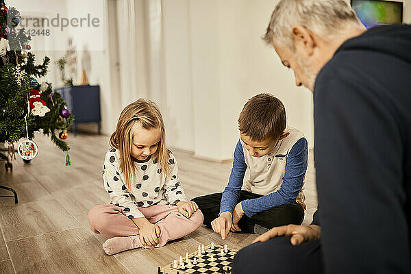 Enkelkinder spielen zu Hause Schach mit Großvater