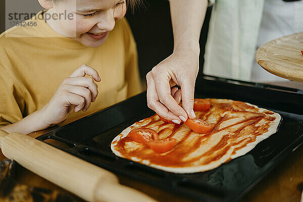 Junge schaut Mutter zu  die Tomatenscheiben auf den Teig im Tablett legt