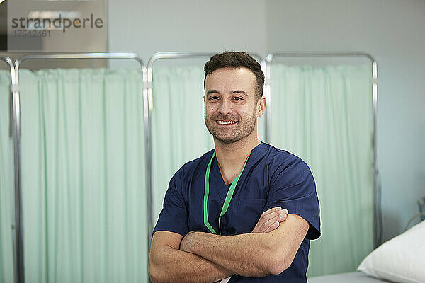 Smiling male nurse with arms crossed in medical room