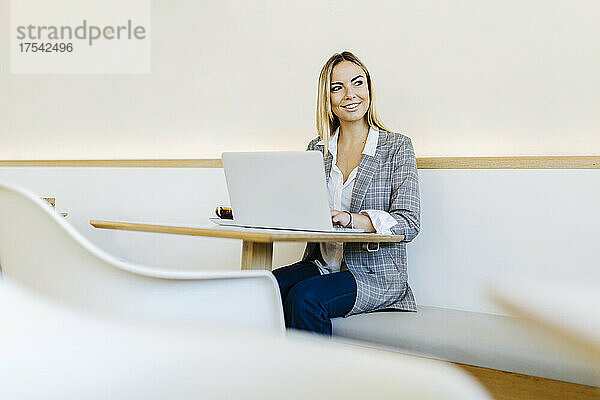 Smiling freelancer with laptop contemplating in cafe