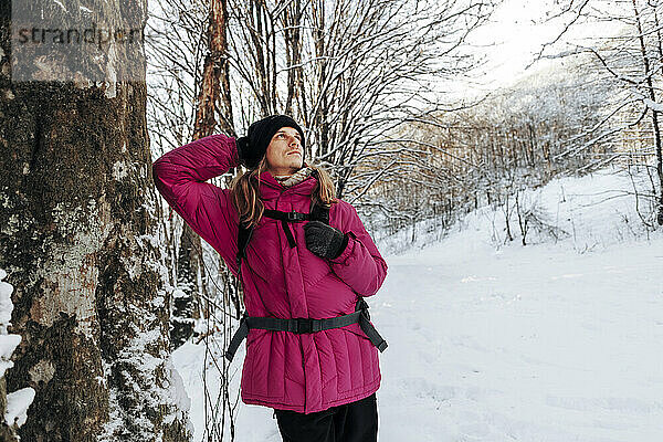 Nachdenklicher Tourist lehnt an Baum im Winterwald